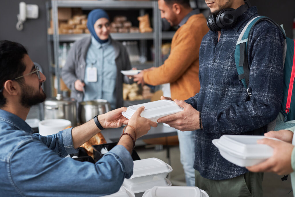 Volunteer Giving Free Food to Middle Eastern Refugees Standing in Line Volunteer Giving Free Food