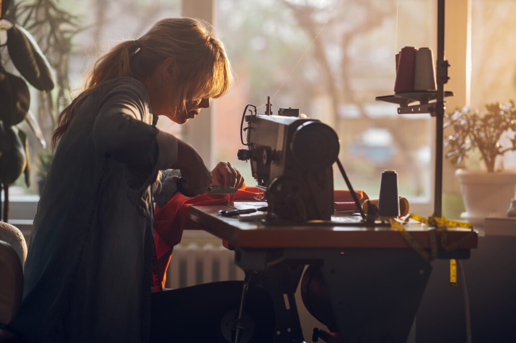 Tailor woman sitting and sewing on a sewing machine a in studio Tailor woman sitting and sewing on a sewing machine a in studio